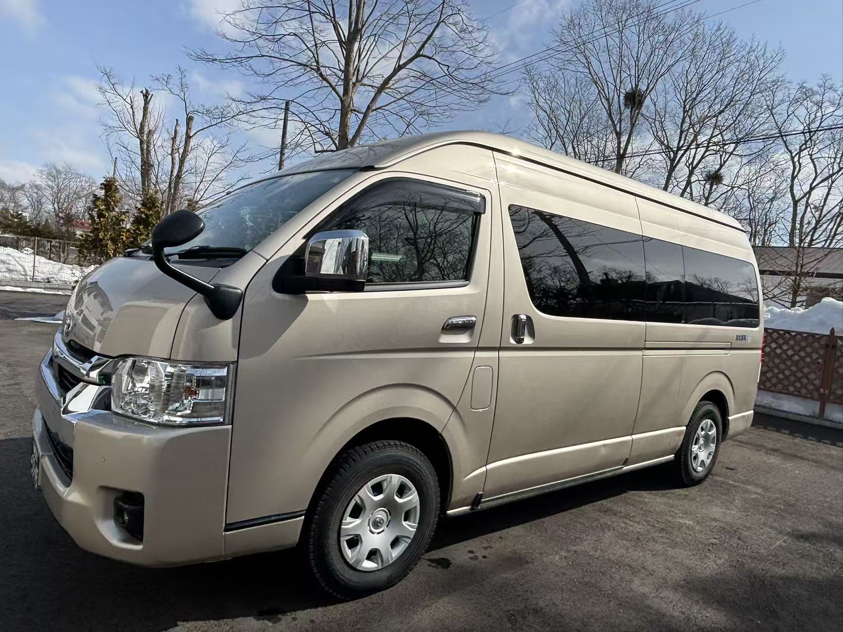 Champagne-pearl Toyota Hiace Grand Cabin group transfer parked at a Hokkaido residence in late winter sunlight