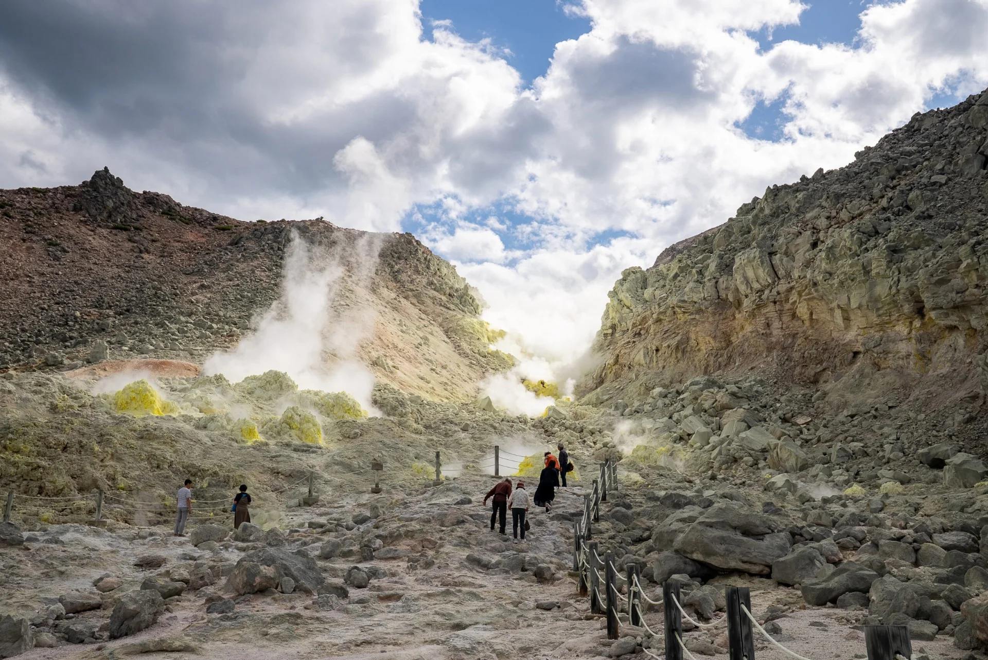 Steam and yellow sulfur vents rising from the rocky slopes of Mt. Iōzan with visitors walking the trail