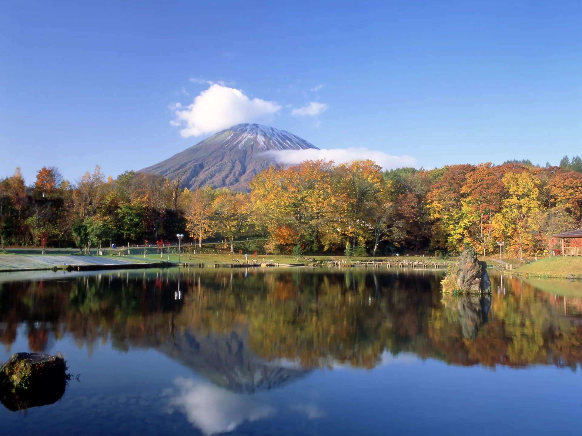 Snow-dusted Mt. Yōtei mirrored in a still lake surrounded by orange and yellow autumn foliage