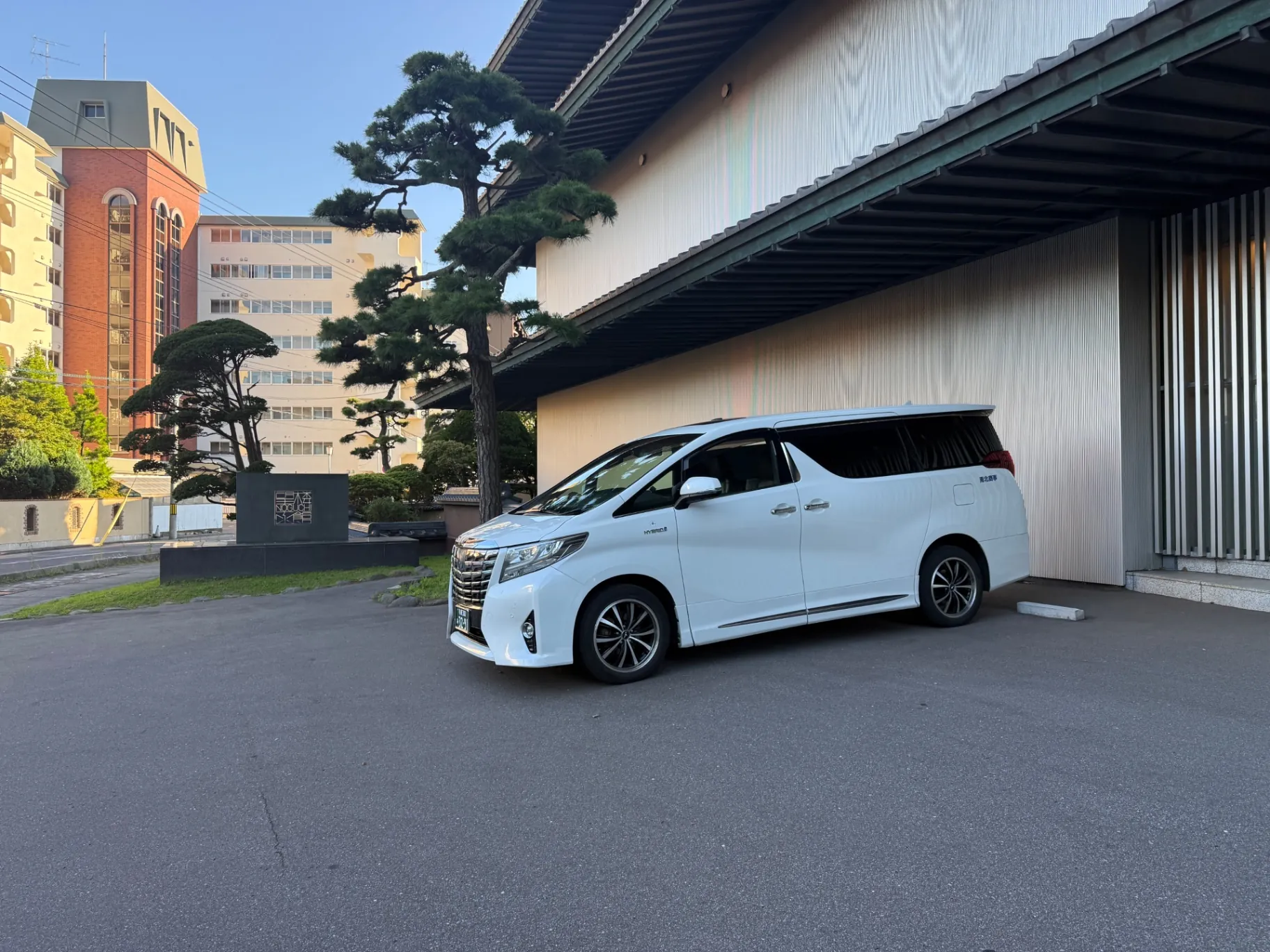 White private van waiting at a traditional ryokan entrance with pine trees