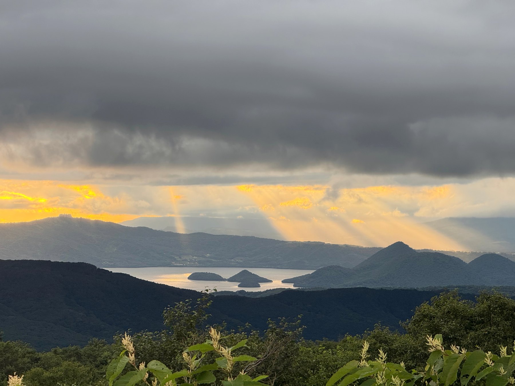 Lake Tōya at dusk, sun rays piercing the clouds above Mt. Yōtei