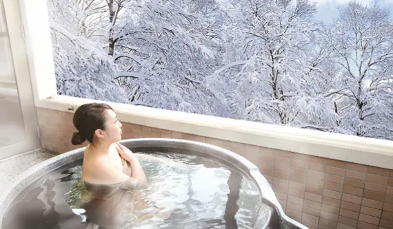 Guest relaxing in an onsen bath with a snowy forest view in Hokkaido