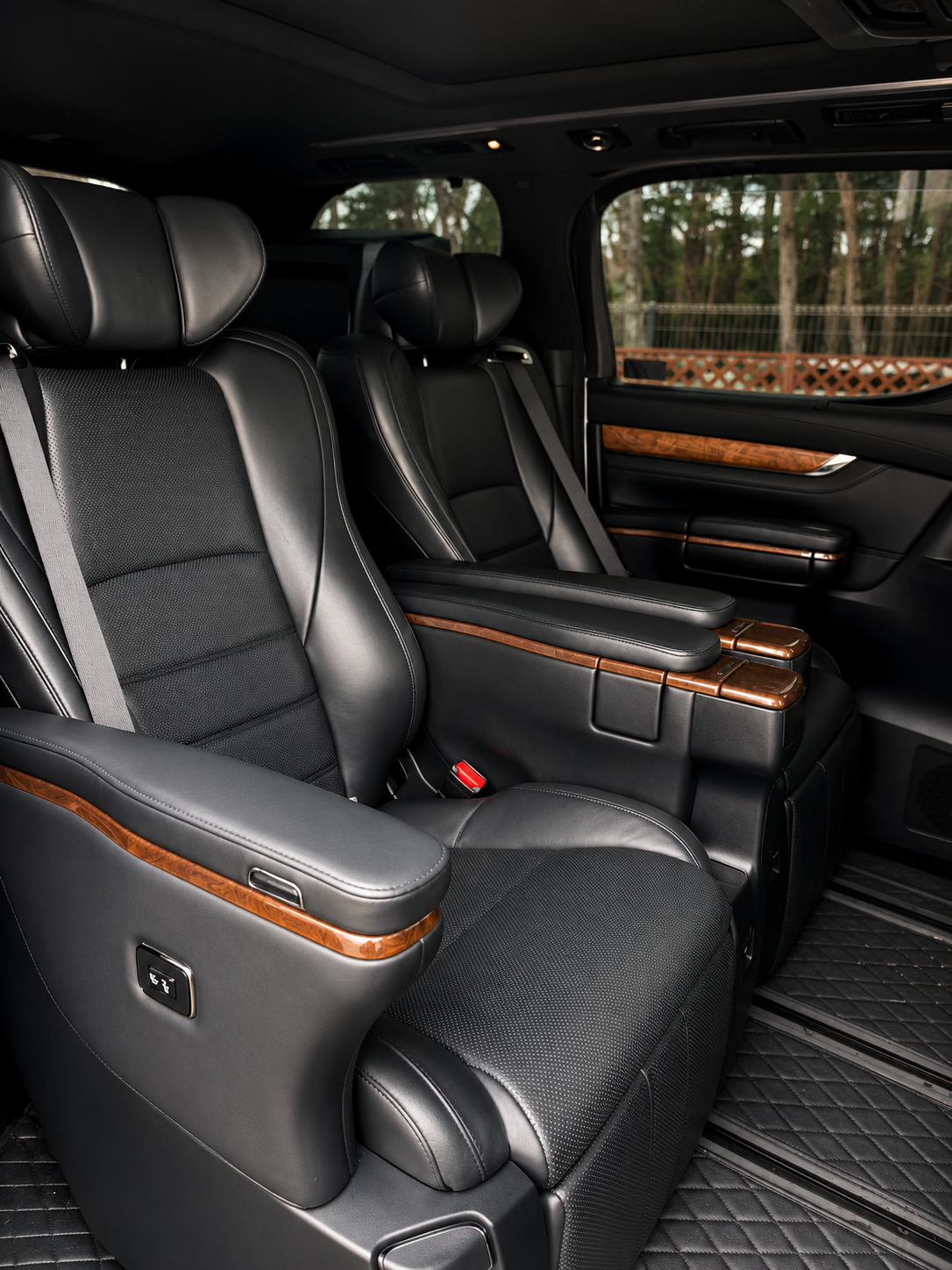 Black leather rear cabin of a Toyota Alphard with wood-trim armrests and panoramic moonroof
