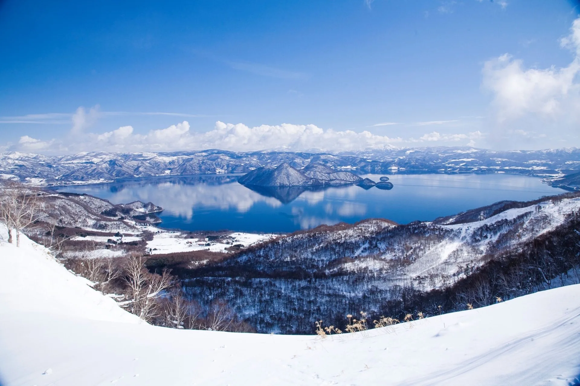Winter panorama over snow-covered Lake Tōya with Nakajima islands and mountains reflected in deep blue water