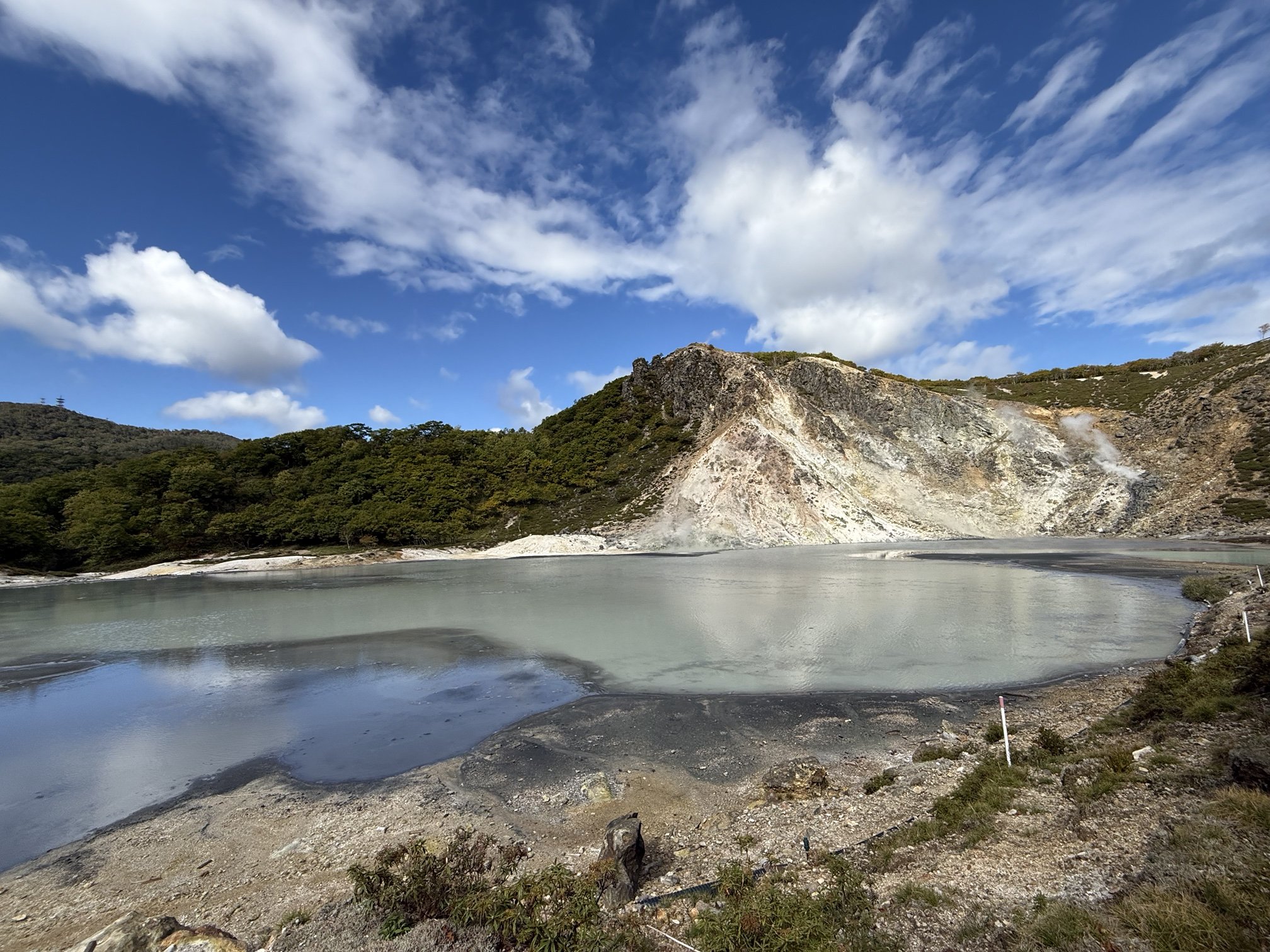 Oyunuma pond in Noboribetsu beneath a blue sky, with steam and a pale volcanic hillside
