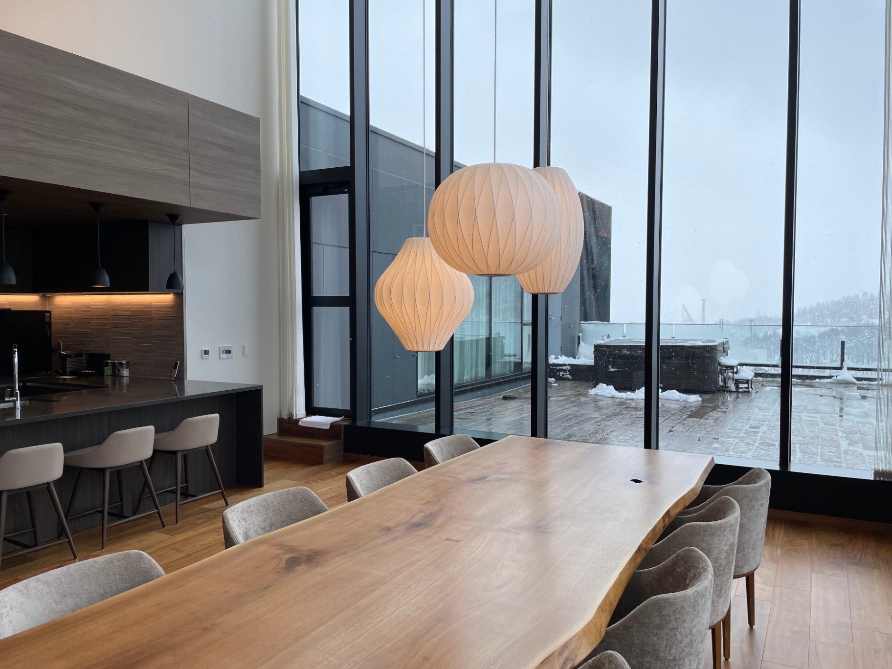 Live-edge dining table in a Niseko penthouse chalet, snow falling beyond the terrace