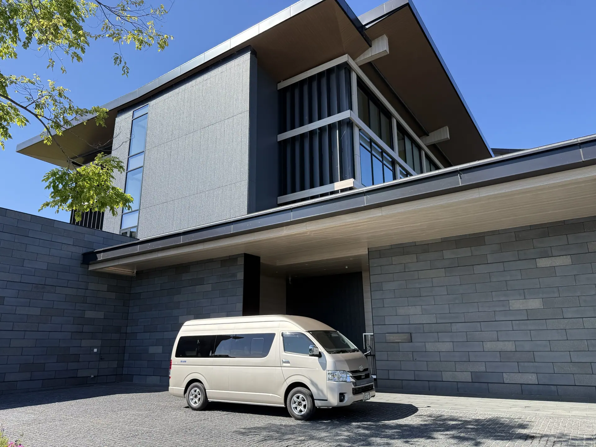 Private van parked at a modern stone hotel driveway under a clear sky
