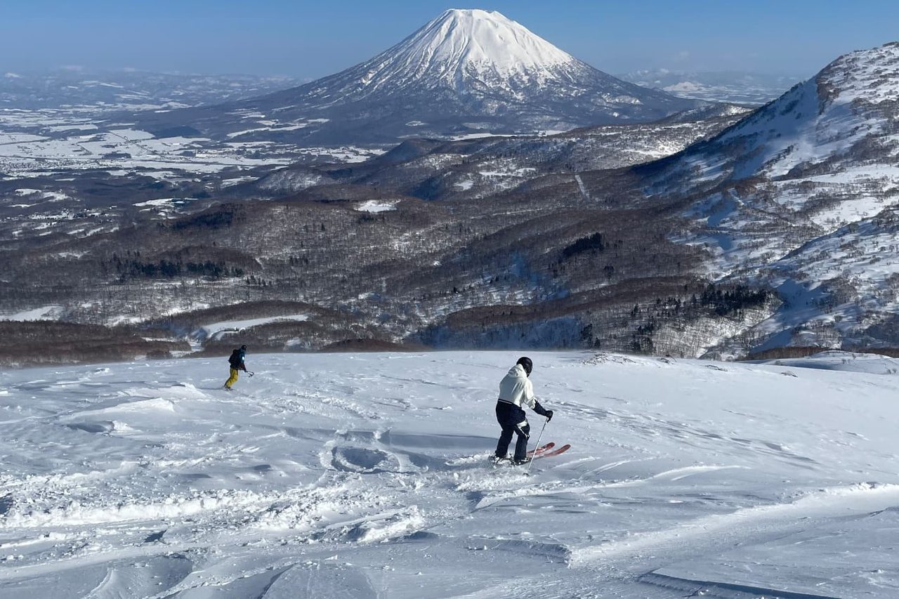 Skiers descending a snowy Niseko slope with Mt. Yotei rising beyond