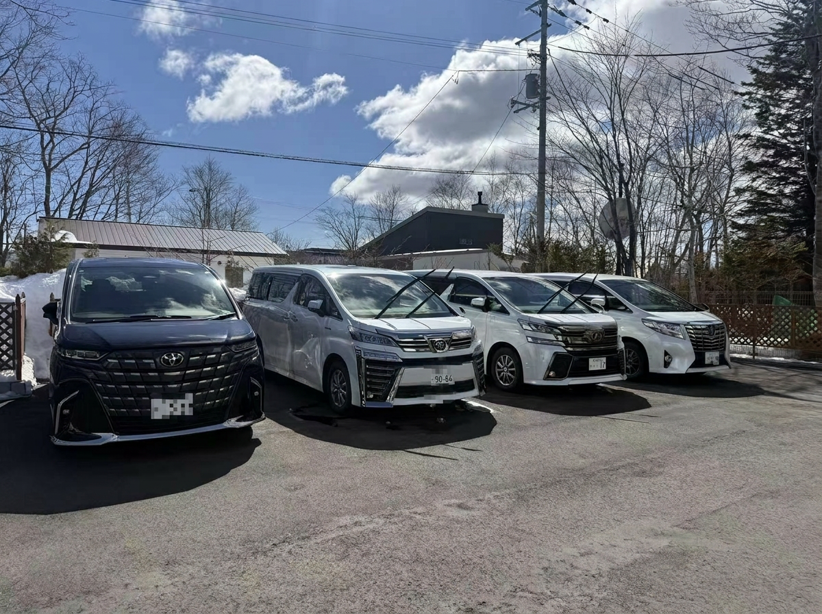 Our Hokkaido fleet — black and white Toyota Alphard / Vellfire executive vans lined up under winter sky (license plates masked for privacy)