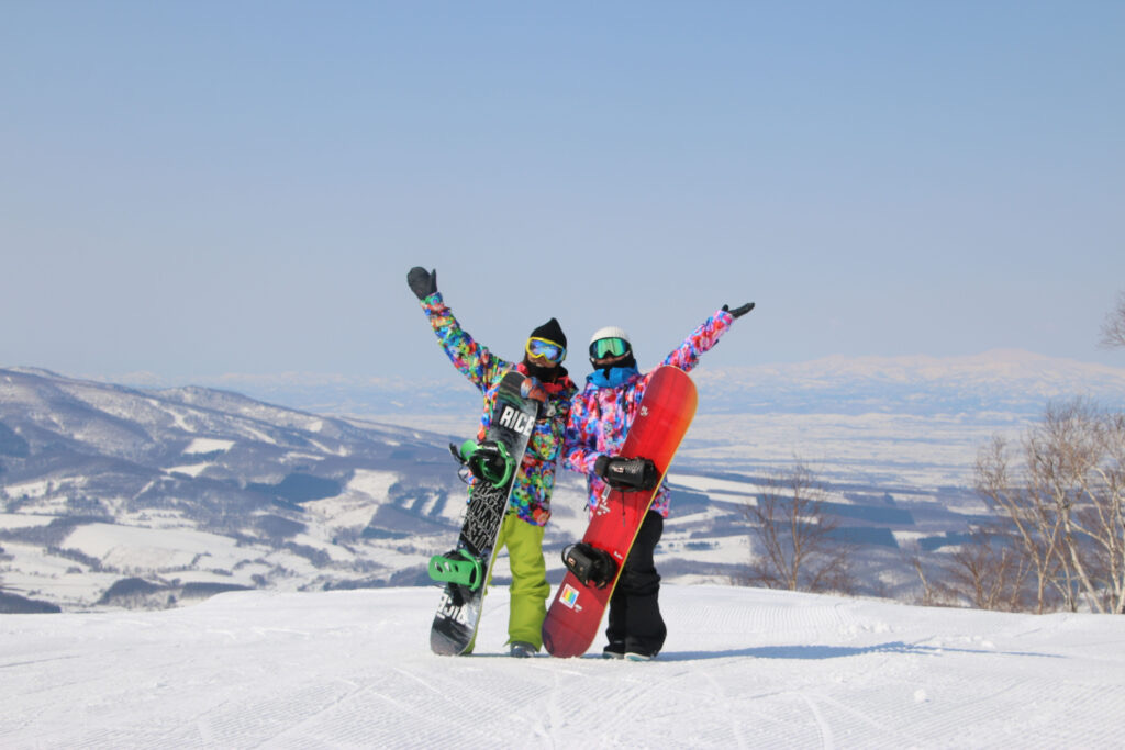 Snowboarders on a Furano summit with valley views