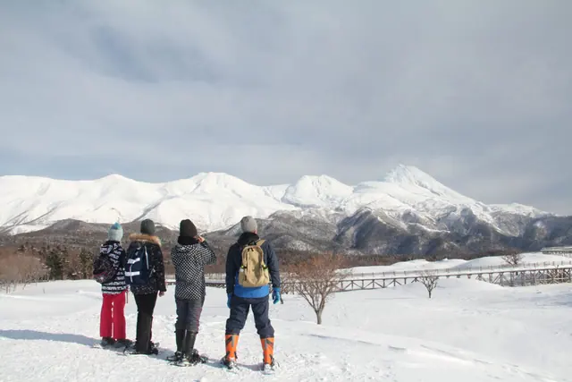 Family on snowshoes looking at snow-covered mountains in Hokkaido