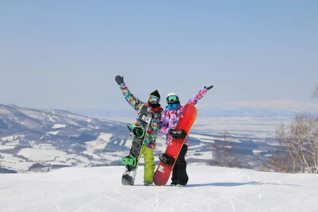 Two snowboarders raising their arms on a snowy summit in Hokkaido