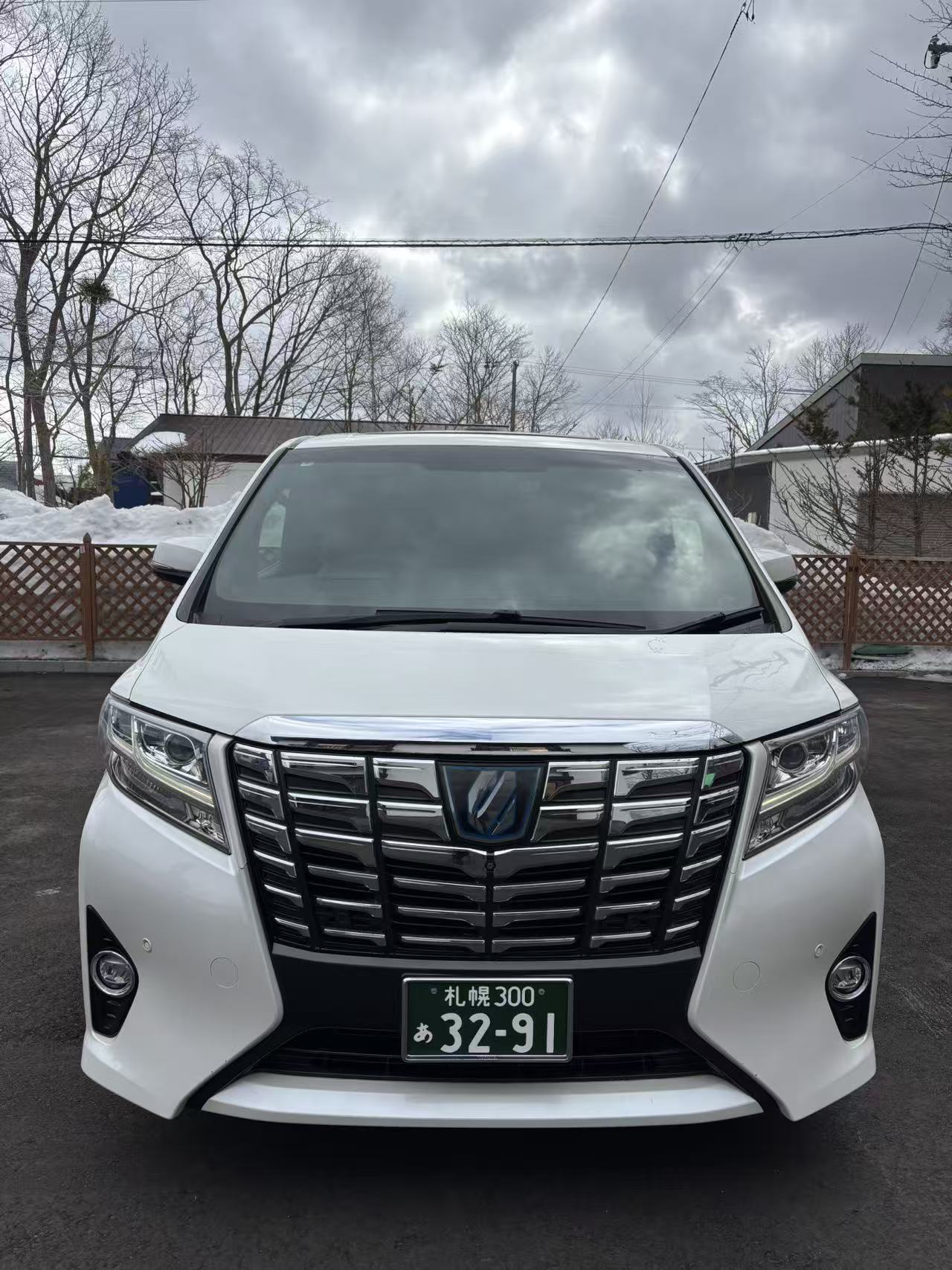 White Toyota Alphard executive private transfer waiting at a quiet Hokkaido residence under a soft snowy sky
