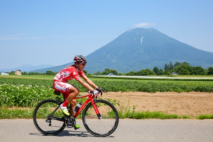 Cyclist riding past summer fields with Mt. Yotei in the background
