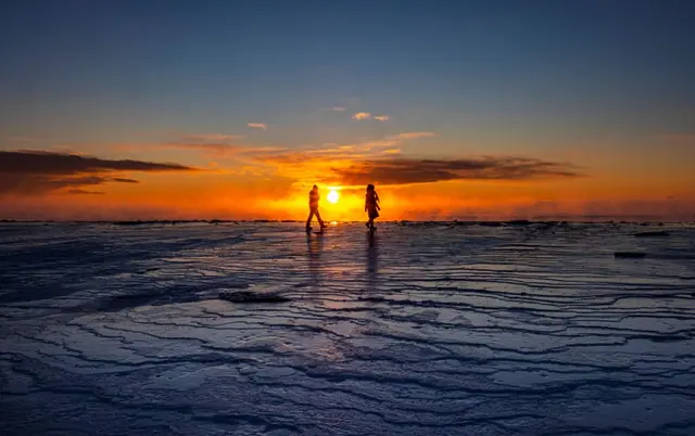 Two people walking on drift ice at sunset in Hokkaido